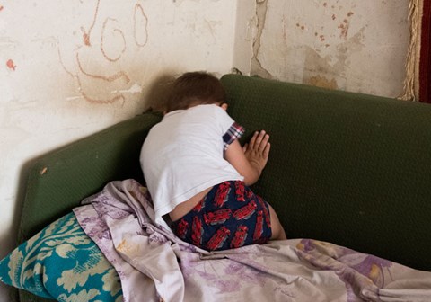 En gutt ligger med ryggen til, krøllet sammen i en sofa. Veggene bak sofaen er slitt. Illustrasjonsfoto: Katerina Ilievska