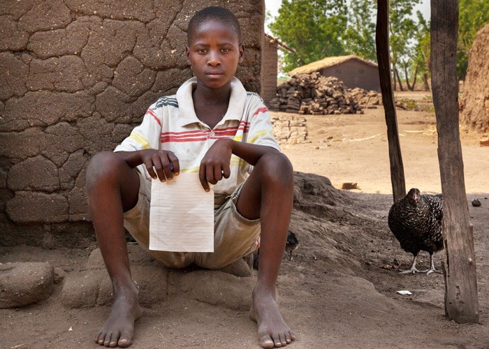 Yonas sitter inntil en vegg og holder en skoleoppgave i hånda. Foto: George Kurian
