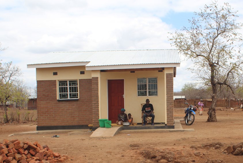 Gladys and her familiy's new house. She and two of her children are sitting outside. Photo: SOS Children's Villages