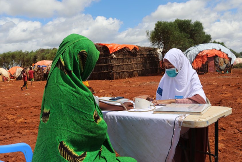 Kvinne i grønn hijab får helsehjelp av en medarbeider fra SOS-barnebyer. Rundt dem er det satt opp provisoriske telt. Foto: Abdulahi Tarmidi
