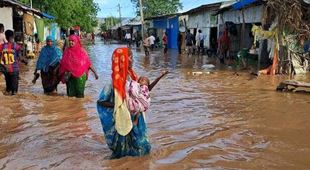 Området rundt husene er oversvømmet av vann. En kvinne bærer et lite barn gjennom vannmassene. Foto: Abdulahi Tarmidi
