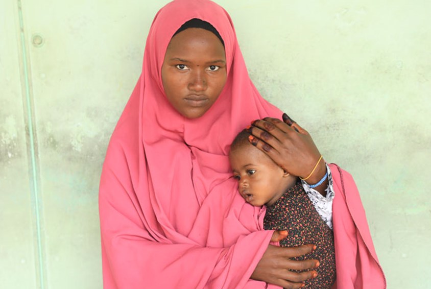 Ung mor, som har måttet flykte fra tørke og sult, sitter med den lille datteren på fanget. Hun har på seg rosa hijab. Foto: SOS-barnebyer
