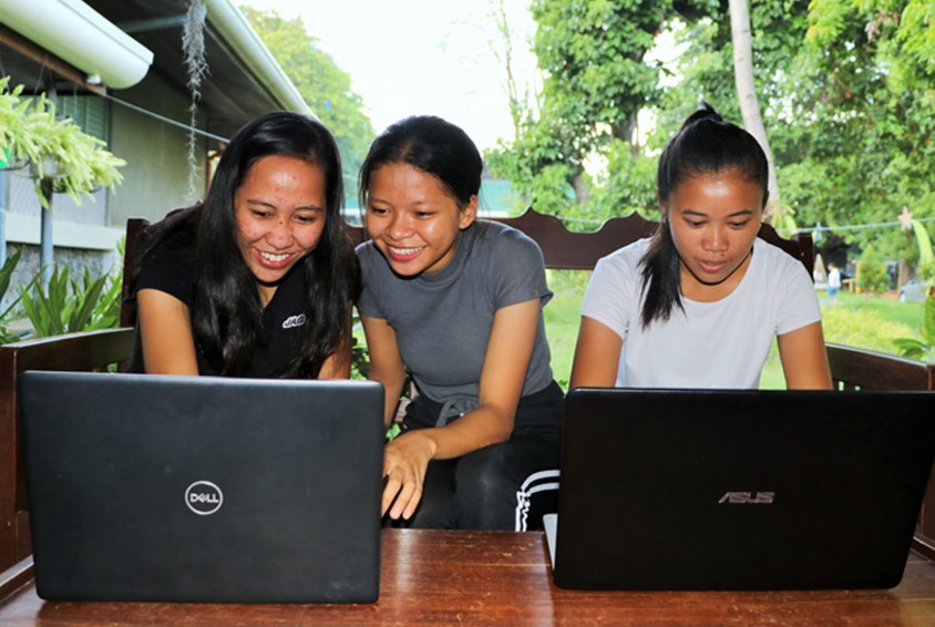 Tre unge fra SOS-barnebyer Filippinene står foran to PCer og smiler. Foto: SOS-barnebyer Filippinene