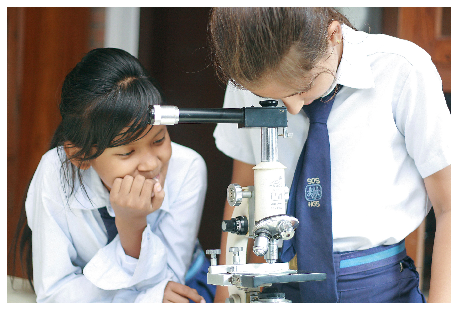To jenter i skoleuniform studier i mikroskopet. Fra en SOS-skole i Nepal.
