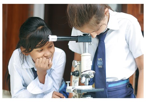 To jenter i skoleuniform studier i mikroskopet. Fra en SOS-skole i Nepal.