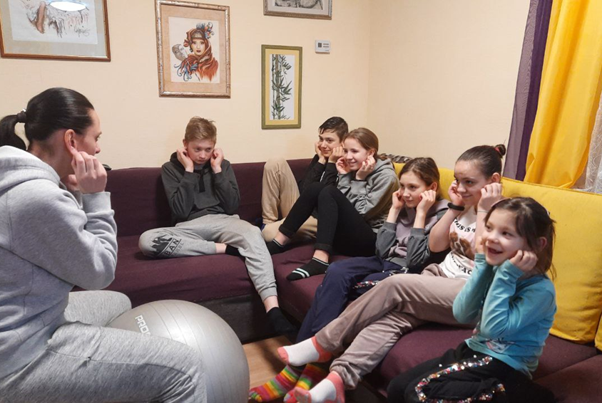 Mellom flyangrepene sitter psykologen ved SOS- barnebyer i Bovary og lærer barn gjennom lek hvordan de skal reagere når flyalarmen går. Barna og psykologen sitter i en sofa. Foto: SOS-barnebyer