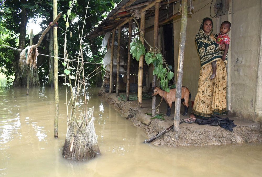 En familie står utenfor hjemmet sitt under flommen i Sylhet i Bangladesh sommeren 2022. Ekstremvær og stigende vannmasser tvang mange familier til å forlate hjemmene sine og starte på nytt. Foto: SOS-barnebyer Bangladesh