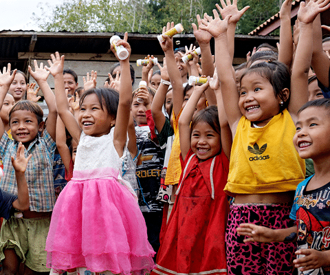 En gjeng med smilende barn i Laos som strekker hendene i været. Foto: Agnete Schlichtkrull