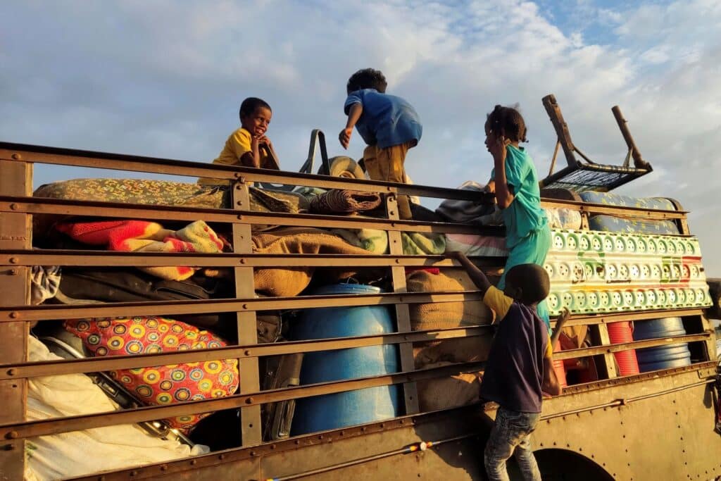 Barn på flukt i Sudan, klatrer opp på lastebil. Foto: AFP