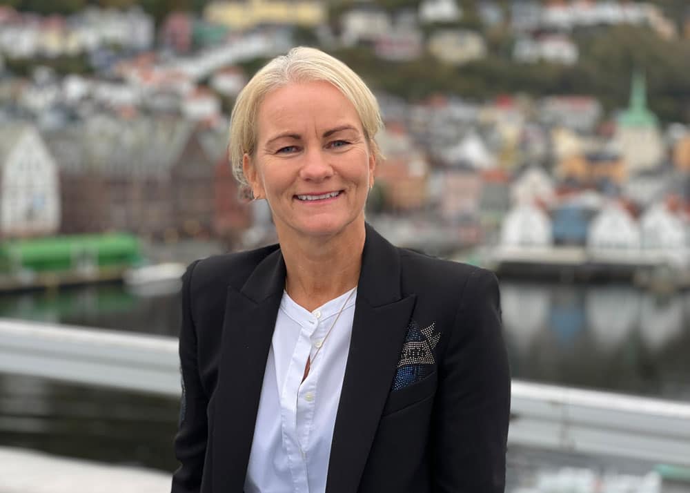 Elna Kathrine Grieg, styreleder Grieg Foundation. Hun står ut og har lang lyst hår i en topp, mørk dressjakke og hvit bluse. Foto Grieg Foundation