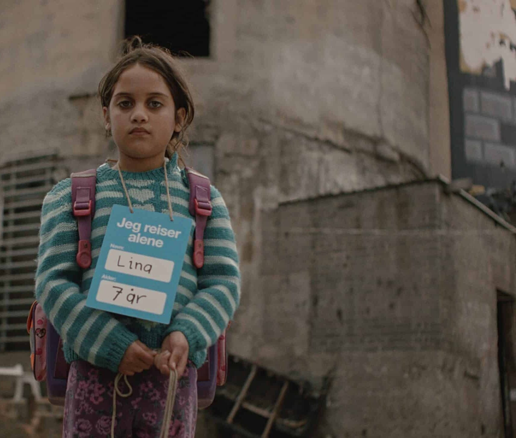 En jente på sju år står ute med et skilt rundt halsen der det står «Jeg reiser alene». Bildet er fra SOS-barnebyers kampanjefilm og symboliserer barn som vokser opp alene i Gaza.