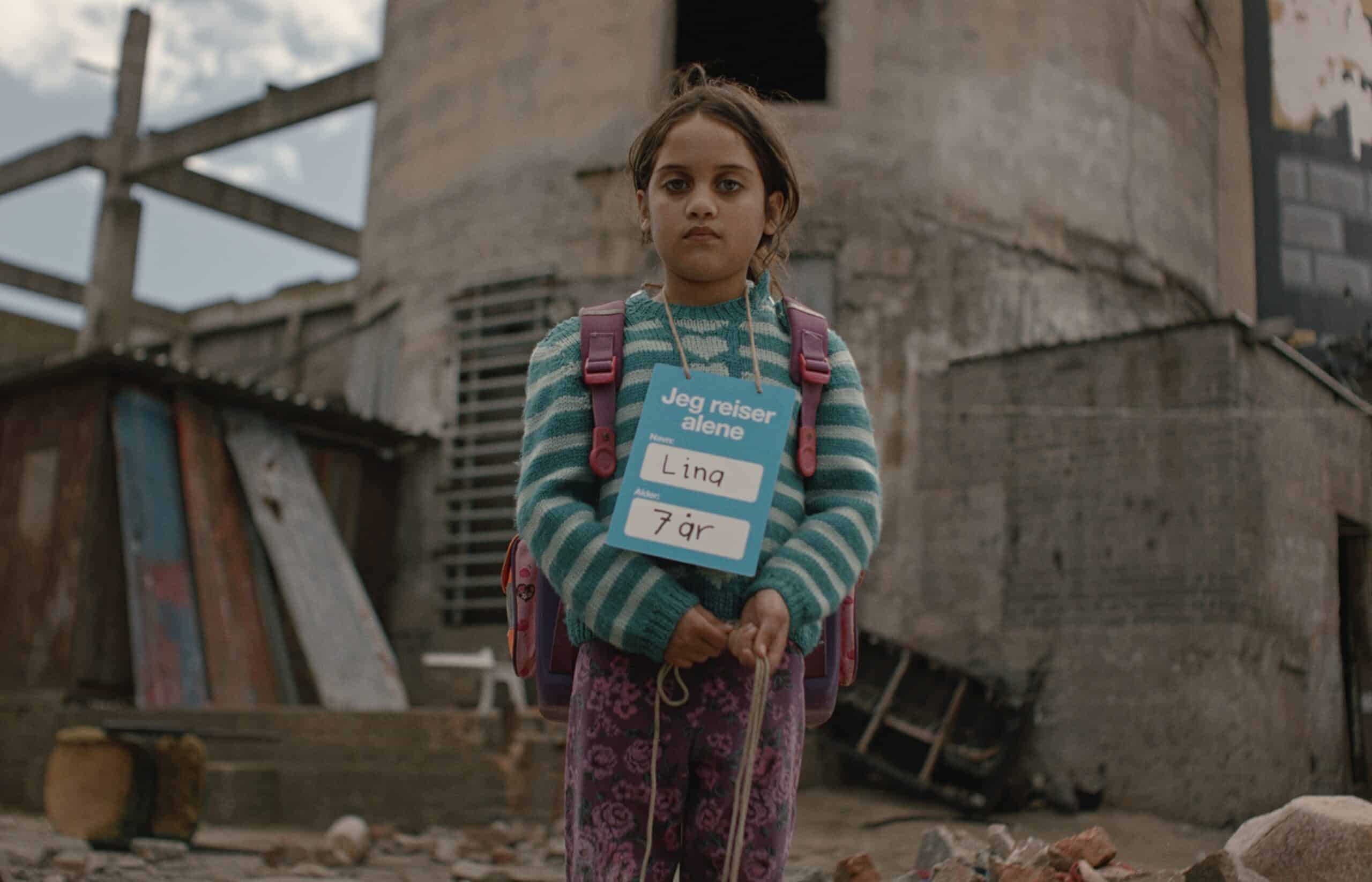 En jente på sju år står ute med et skilt rundt halsen der det står «Jeg reiser alene». Bildet er fra SOS-barnebyers kampanjefilm og symboliserer barn som vokser opp alene i Gaza.