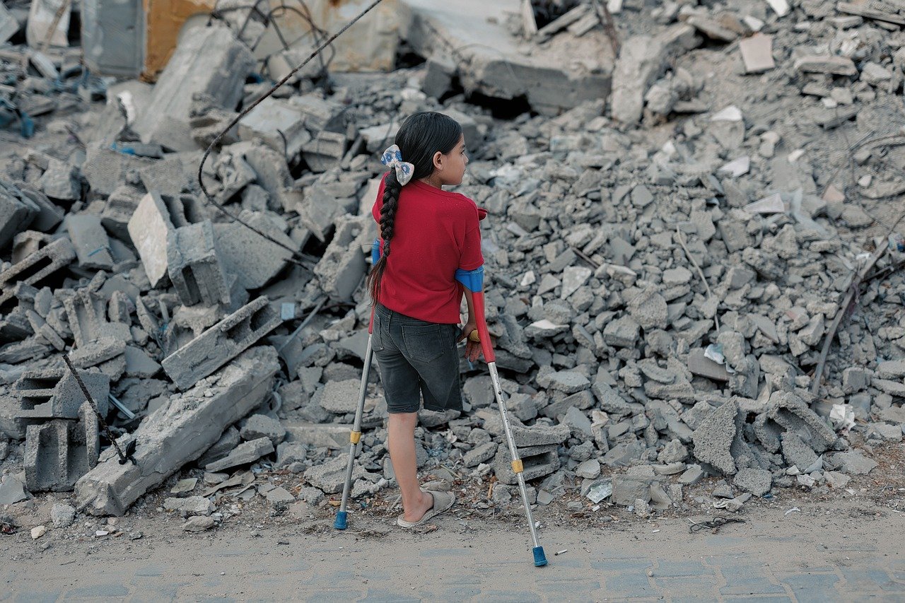 Jente med én fot og krykker som står og ser utover ruinene i Gaza