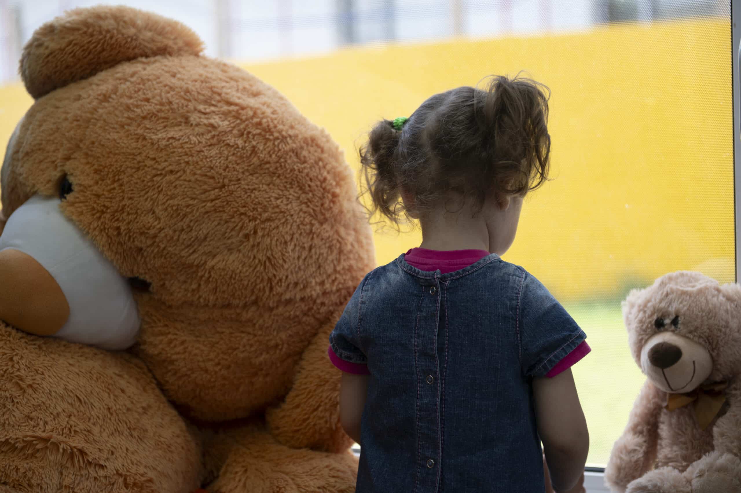 Alina står med ryggen til og ser ut av et vindu sammen med kosedyr i Borodjanka i Ukraina.