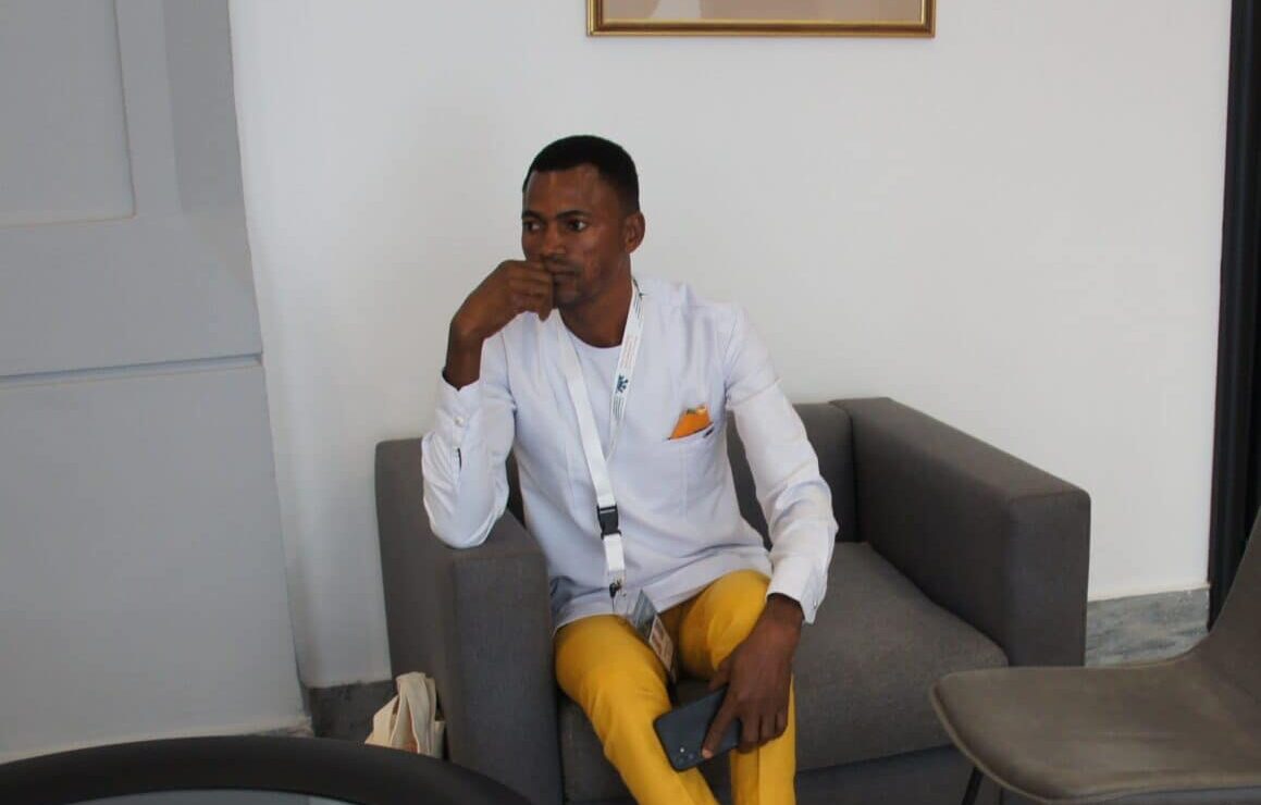 Wisdom sitter i en stol i et kontor mens han holder i telefonen sin