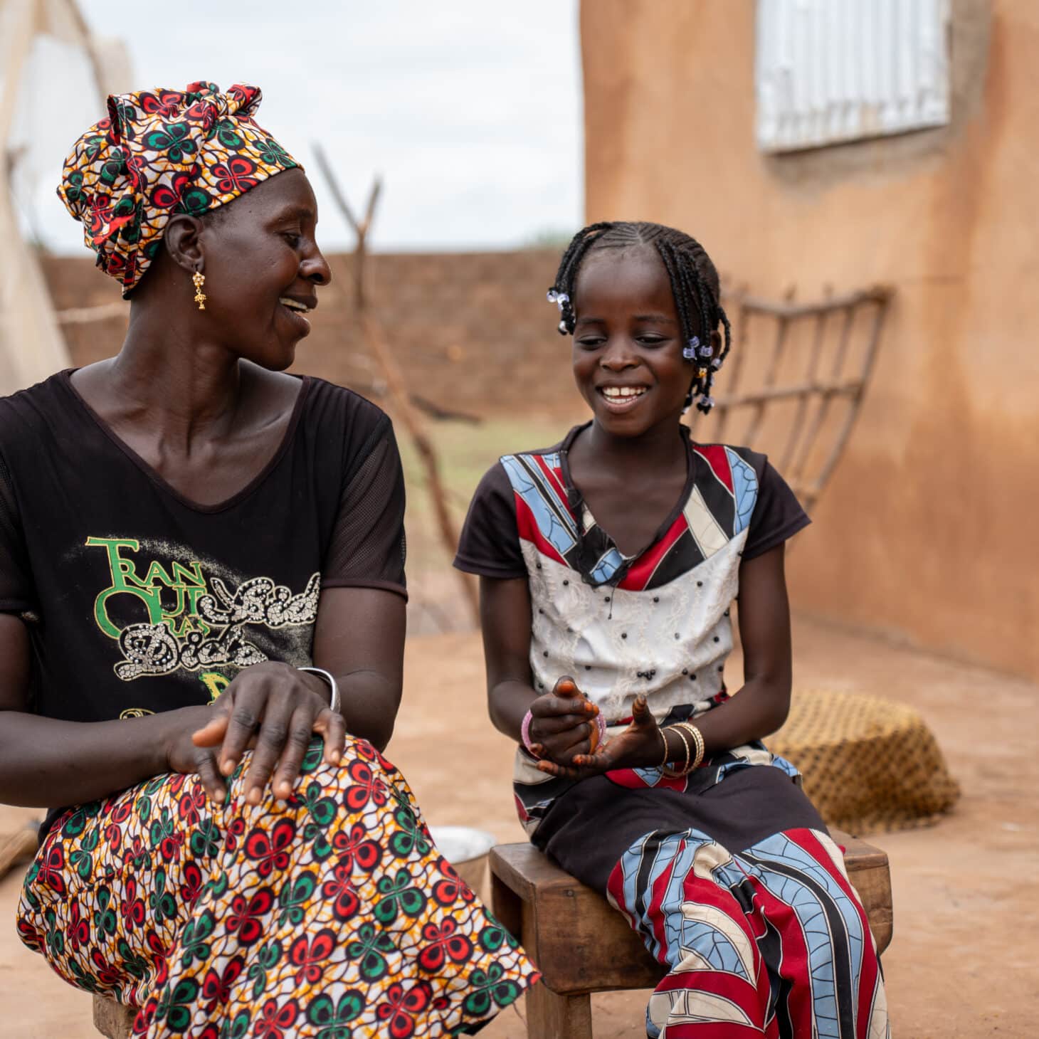 Dador og den yngste datteren hennes sitter sammen utenfor hjemmet i Makka Farafenni i Gambia og smiler til hverandre.
