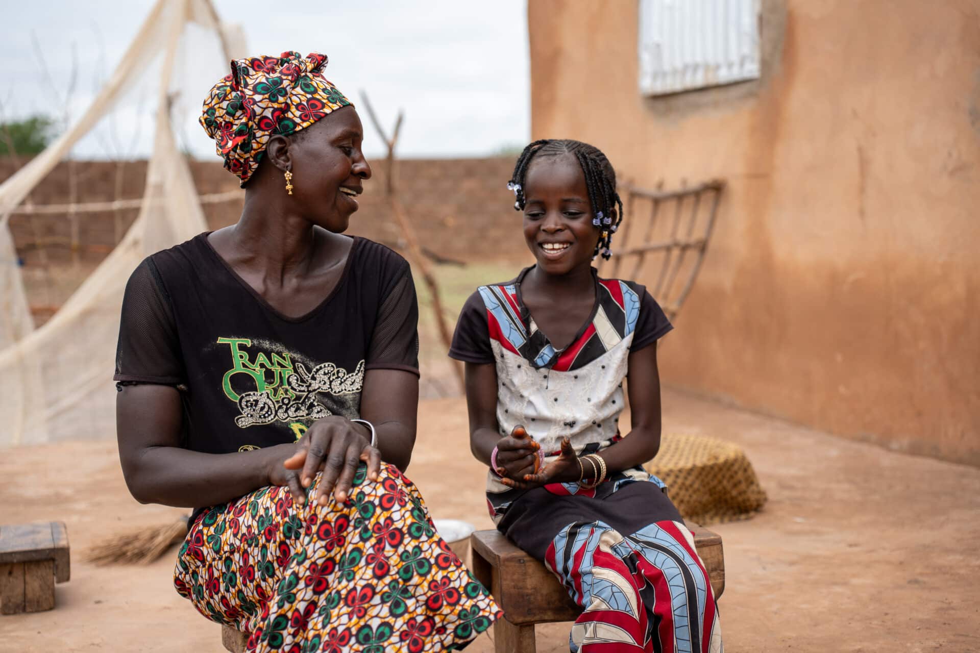 Dador og den yngste datteren hennes sitter sammen utenfor hjemmet i Makka Farafenni i Gambia og smiler til hverandre.