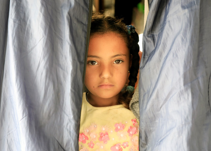 Jente med et alvorlig uttrykk i ansiktet, tittet ut i teltåpningen. Foto Giorgos Moutafis
