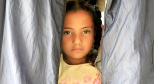 Jente med et alvorlig uttrykk i ansiktet, tittet ut i teltåpningen. Foto Giorgos Moutafis