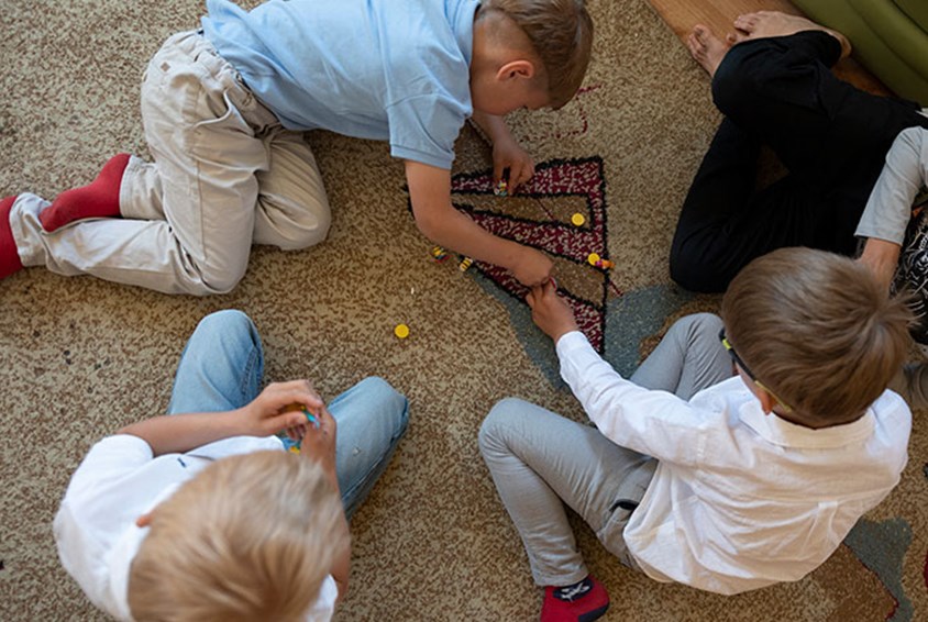 Tre gutter sitter på gulvet og spiller et brettspill. Illustrasjonsfoto: Katerina Ilievska