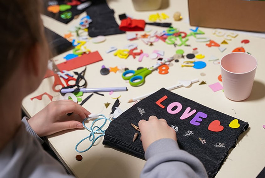 Ei jente sitter ved et bord og limer fargerike hjerter og bokstavene LOVE på et svart ark. Illustrasjonsfoto: Lydia Mantler