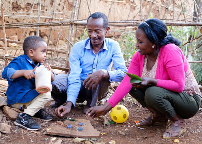 Zelalem sitter på bakken sammen med fosterforeldrene og leker. Foto: Jakob Fuhr