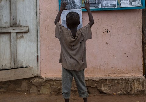 En gutt med hullete t-skjorte står å ser på en vegg med plakater. Han strekker armene i været. Illustrasjonsfoto Conor Ashleigh