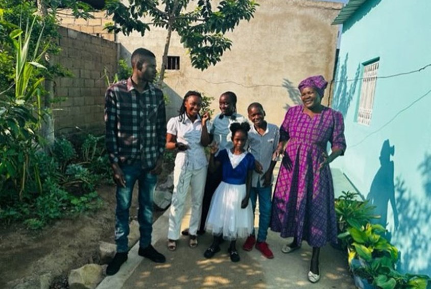 SOS-mor Ceciilia i lilla kjole står foran huset sammen med barna, tre jenter og to gutter. Foto: SOS-barnebyer
