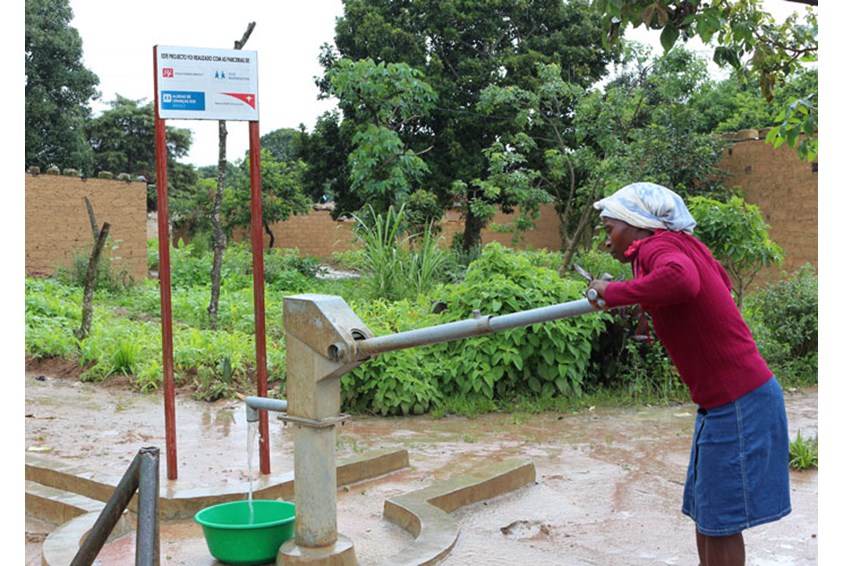 Isabel med hvitt skaut, rød skjorte og blått skjørt pumper vann i en stor balje. Foto: SOS-barnebyer