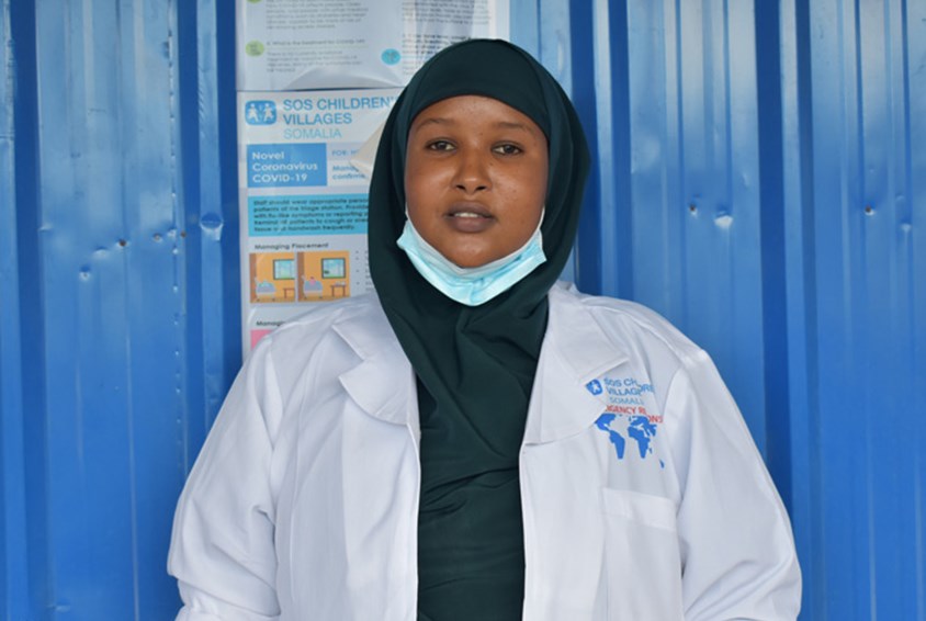 Sykepleieren Halima Ahmed Dalel står foran en blå vegg. Hun jobber hardt for å lindre smertene til de som har mistet alt. Foto: Fadumo Ali