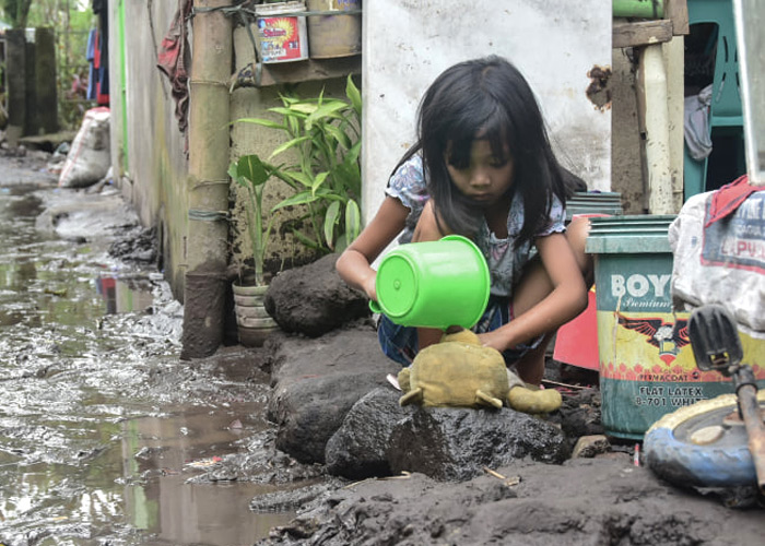 Jente sitter og leker med bamsen sin utenfor huset der veien er full av vann og gjørme. Filippinene. Foto Philip Llorera Moico