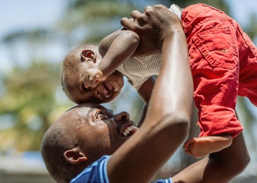 En smilende pappa fra Mosambik løfter barnet sitt i været.
