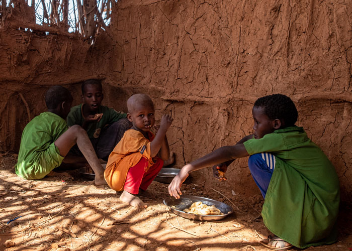 Barn sitter inne i et hus lagd av leire med utett tak og spiser injera. Foto: Joost Bastmeijer