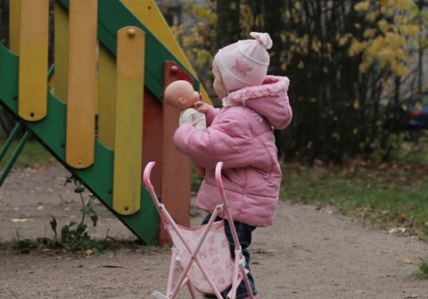 Ei lite jenta i Russland i rosa uteklær med en dukke og en vogn. 