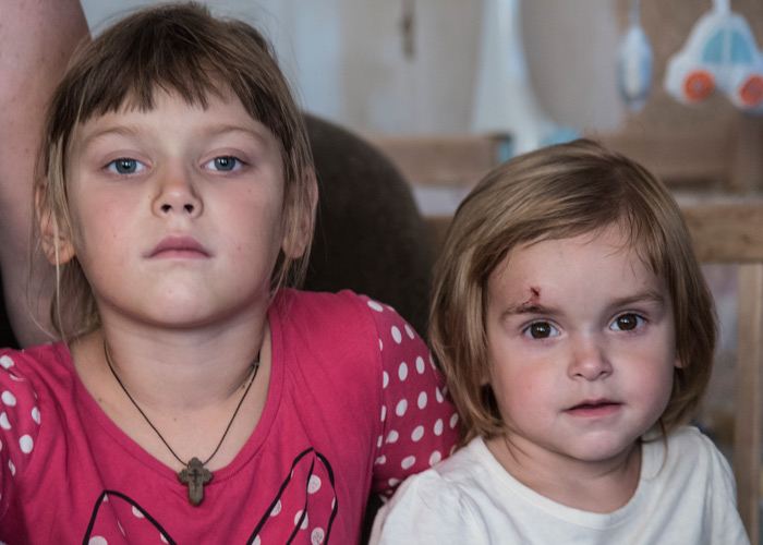 Bilde av to søstre fra Ukraina. Sitter på sofaen og ser rett i kamera. Alvorlig blikk på begge. Foto: Katerina Ilievska