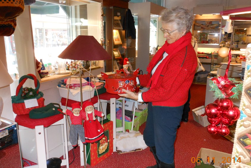 En dame med rød genser står i bruktbutikken i Fredrikstad med mange juleartikler.