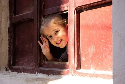 Bilde av en liten jente som titter ut av et vindu.