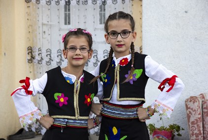 To jenter i hvite bluser med sort vest med broderte fargerike blomster på.