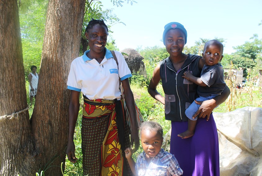 Familie fra Mwanza Tanzania; mor til venstre med hvit t-skjorte, datter til høyre med sort t-skjorte og et lite barn på hofta. Et lite barn står foran i midten.