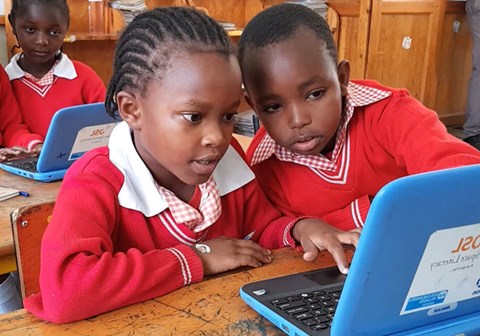 Ei jente og en gutti skoleuniform, rutet skjorte og rød genser, sitter ved samme pult og jobber med PCen. Fra en SOS-skole på det Afrikanske kontinentet. Foto: Ahmed Mihaimeed