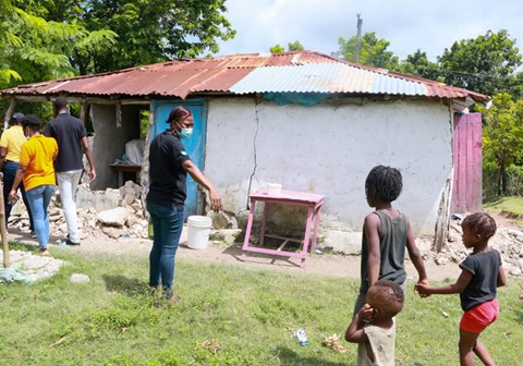 Medarbeider fra SOS-barnebyer i Haiti strekker ut hånda mot tre barn som er utenfor et hus rammet av jordskjelvet, med store ødeleggelser. Foto: Joubert Rochefort