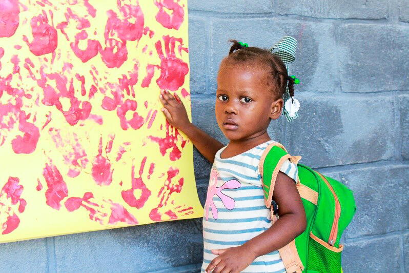 En jente som får støtte gjennom SOS-barnebyer poserer foran tavlen. Foto SOS-barnebyer