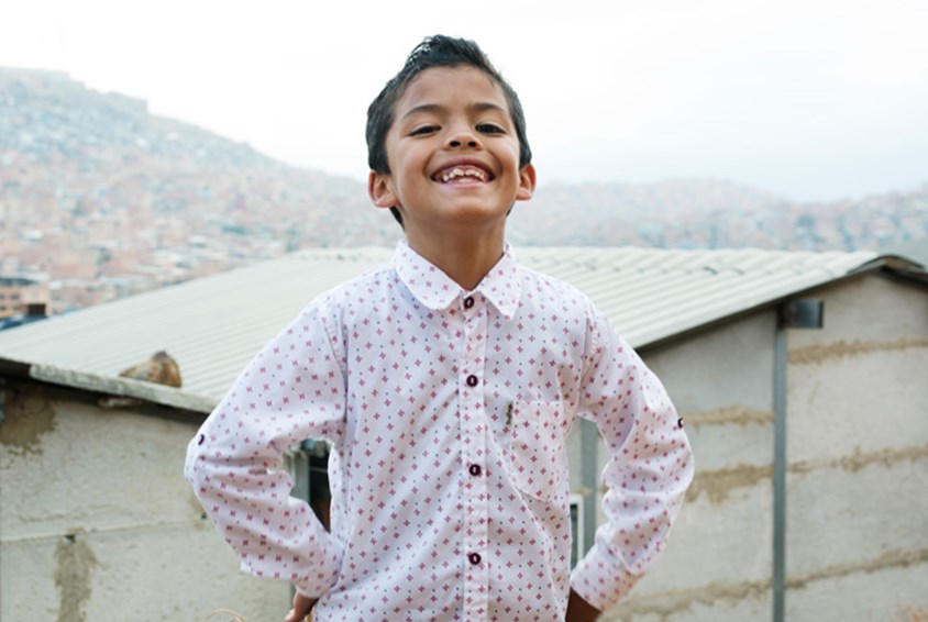 Gutt som bor i Bogota, Colombia, står med hendene i siden og smiler. Foto: Nina Ruud