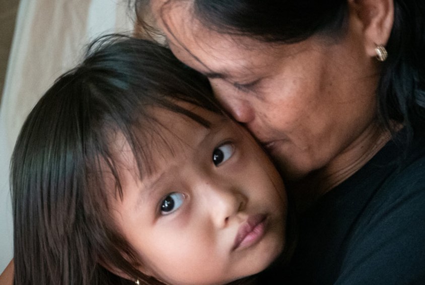 Mor fra Filippinene holder datteren sin i armene og klemmer henne.