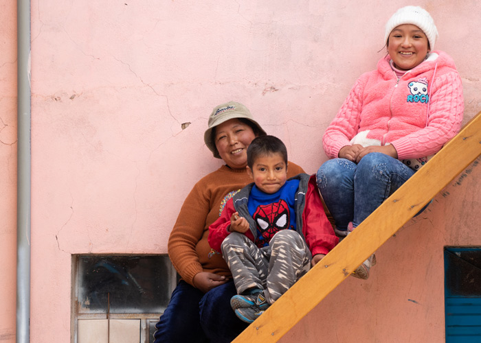 Peru: Mor, med sønnen på fanget, og datter sitter i ei trapp. Veggen bak er rosa. 