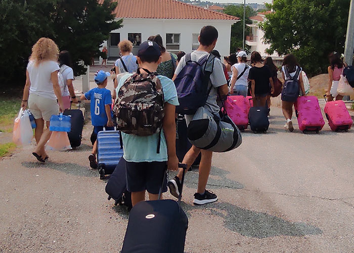 Barn og ansatte fra SOS-barnebyen Thrase i Hellas ankommer barnebyen Plagiari, som går fra bussen mot hovedhuset i barnebyen, alle har en koffert med seg. Foto: SOS-barnebyer Hellas