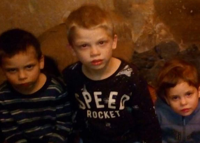 Tre søsken fra Ukraina sitter på en madrass i et bomberom og ser alvorlig inn i kamera. Foto: SOS-barnebyer