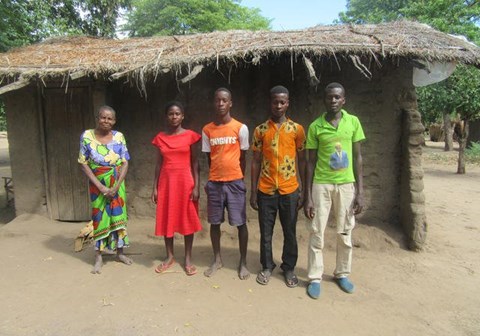 Kozani med brødrene og bestemoren sin. De står utenfor huset sitt, som er av leire og har stråtak. 