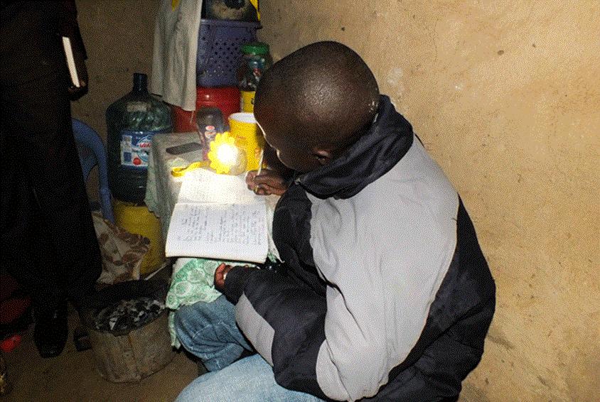 Gutt sitter i et rom og leser lekser, det er upussete murvegger og kun et lite lys. Illustrasjonsfoto: Catherine Ochung