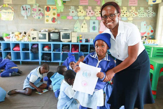 Ei lita jente viser stolt fram det hun har tegnet. Lærer Mhako står bak henne. Foto: Tom Maruko